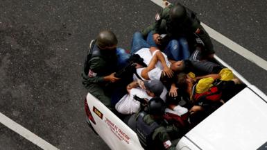 Bolivarian National Guard officers bundle demonstrators into the back of a pickup truck following protests