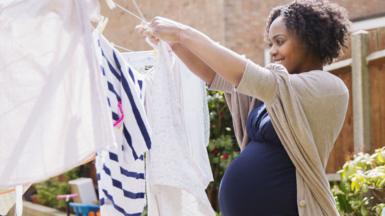 A young pregnant black woman puts out washing on washing line on a sunny day in a garden