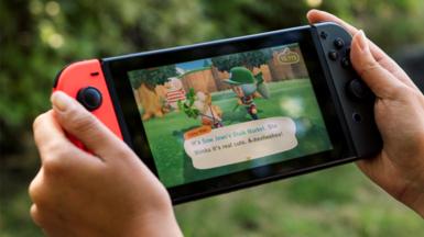 Close up of hands playing Animal Crossing: New Horizons on a Nintendo Switch game console