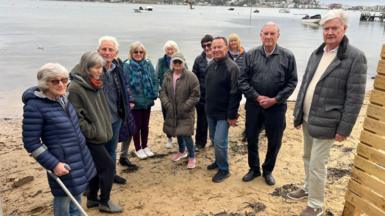 The group of residents who are against the fence stood next to it and on the beach near the water.