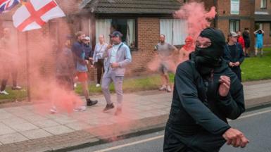 A demonstrator throws a smoke flare at police as Far-right activists hold an Enough is Enough protest in Sunderland on August 02, 2024 in Sunderland, England