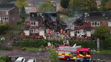 Firefighters on site at the explosion. The houses in the centre have been ripped apart and there is debris on the ground. 