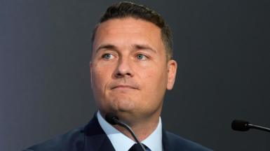 Defence Secretary Wes Streeting speaking at the Farnborough International Airshow in Hampshire. He is wearing a dark blue suit, pale blue shirt, and black tie.