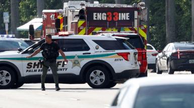 A police officer gestures in front of a sheriff's vehicle and a fire engine, with other cars to the right of frame, in West Palm Beach, Florida, U.S. September 15,