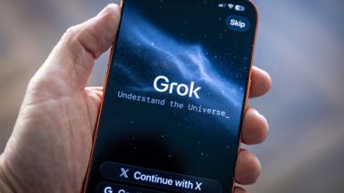A hand holding up a phone with the words "Grok. Understand the Universe" on it against a space background.