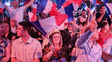 National Rally supporters fly French flags as the results of the first round of voting come in.
