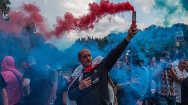 A man holds a flare during a protest outside The Bell Hotel on July 31, 2025 in Epping, England.