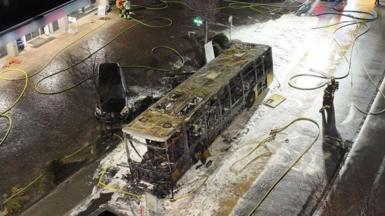 View from above the incident showing burnt out bus surrounded by foam and fire hoses in central area of town.