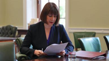 Chancellor Rachel Reeves in a navy blue suit sitting down looking at a speech written on paper