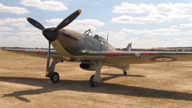 A Hurricane plane standing on dried yellow grass.