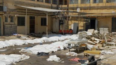 White plastic sheets cover bodies in the carpark of a hospital in Suweida. There is debris of chairs and hospital beds scattered across the ground too