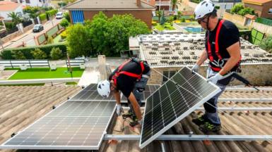Workers install solar panels on a roof