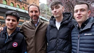 Sir Gareth Southgate stands with three young men. His arms are round the two closest to him
