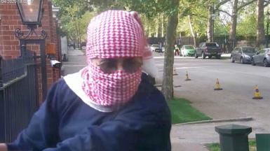 Abdullah Albadri, his head wrapped in a red and white traditional Arabic scarf, holding onto the railings at the Israeli embassy and looking in the direction of diplomatic protection officers - who are out of shot - and who are about to arrest him.