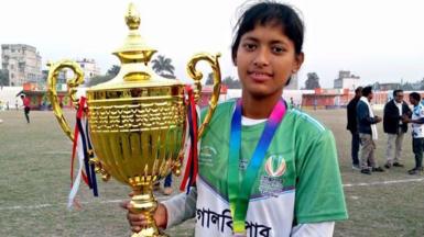 A young woman wearing a medal holds up a trophy