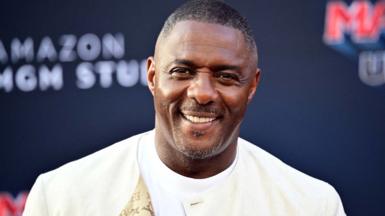 Luther Idris in a cream jacket and white T-shirt
