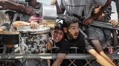 Palestinians carrying pans gather to receive hot meals from a charity kitchen in Gaza City, northern Gaza (23 July 2025)