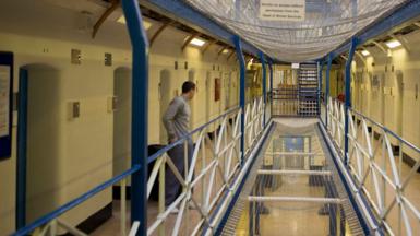 A male inmate looks down an empty prison corridor