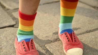 legs of a person wearing rainbow sicks and pink shoes on a plain gray pavement