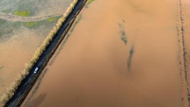 An aerial shot showing a car driving between flooded fields near the River Tone in Somerset. The fields are almost completely invisible under brown floodwater