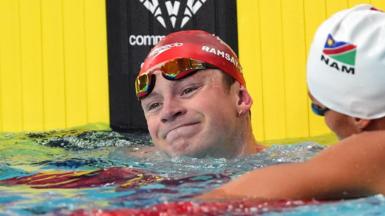 Adam Ramsay-Peaty with his head above water and goggles pulled up to his forehead as he wears a red swimming cap bearing his name