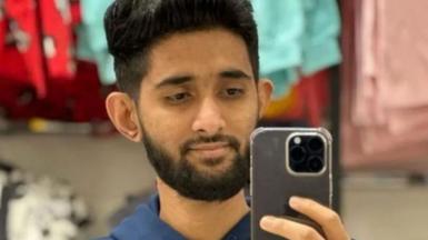 Man with dark hair and dark beard holds up a phone which he is looking into