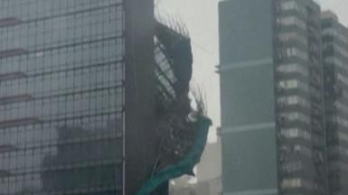 Bamboo and green plastic sheeting are seen falling down the side of a glass skyscraper.