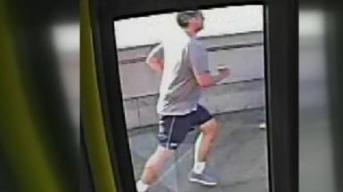 CCTV still image from the inside of a bus showing a man in a grey T shirt and shorts running. 