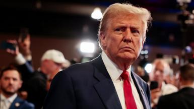 Donald Trump looks away from camera with people in background while in the spin room