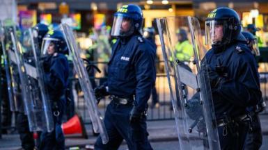 Police officers with riot shields walk along a road in Epsom.
