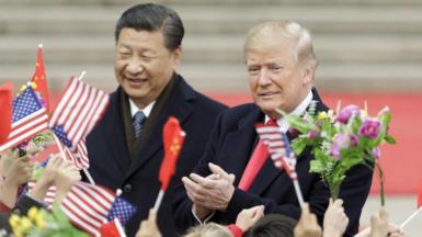 US President Donald Trump, right, and Xi Jinping, China's president, greet attendees waving American and Chinese national flags during a welcome ceremony outside the Great Hall of the People in Beijing, China, on Thursday, 9 November, 2017