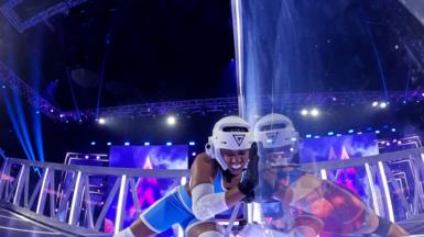 Emily Bell taking part in a challenge on Gladiators. She is wearing a blue outfit and wearing a white helmet and gum shield.