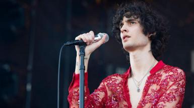 A singer with long dark hair, wearing a see-through red shirt, hold a microphone