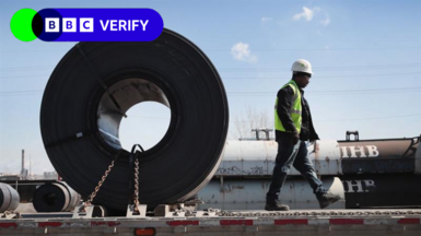 An image of a construction worker walking with a big circular object behind him 