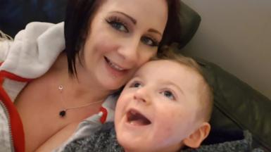 A smiling Bradley Nelson sits with his mother Sharon Boocock on a sofa. 