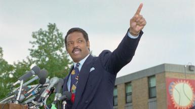 Jesse Jackson points into the air. He is wearing a blue suit. 