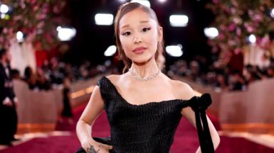 Ariana Grande appears on a red carpet in January wearing a black dress.