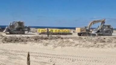 Two excavators are pictured on either side of a set of yellow blocks on sandy ground in Gaza