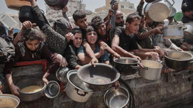 Palestinians hold out pots and bowls, jostling to reach the front of a line as they await meals distributed by aid groups in Gaza City