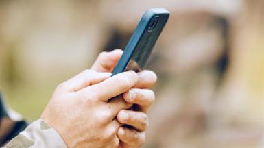 A pair of hands holding a mobile phone, with a camouflage cuff showing. This is a stock image showing a model.
