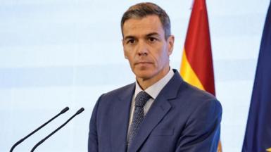 Pedro Sanchez, who has a neutral expression and short greying brown hair, wears a suit and tie as he listens during a press conference