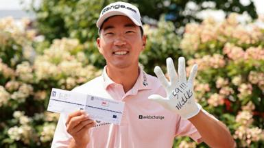 A smiling Michael Kim celebrates his round of 59 by holding up his scorecard and glove with the words '59' on it with three exclamation marks