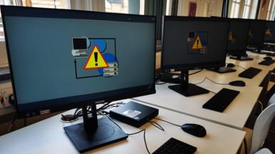 Computer screens on desks showing blue screens with a yellow triangle with an exclamation mark in