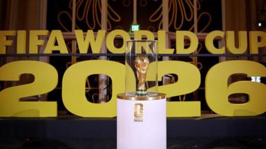 The World Cup on display on a white stand prior to the draw in December in Washington with Fifa World Cup 2026 in big gold letters in the background.