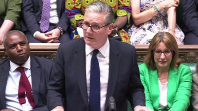 Sir Keir Starmer standing in the House of Commons, flanked by David Lammy and Rachel Reeves. 