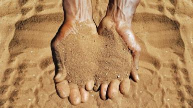 Close-up overhead view of the wrist and hands of an adult male cupping the golden sandy soil of Limpopo Province, South Africa.