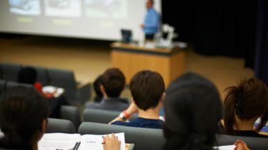 A stock image of a group of university students sat in tiered seating in a lecture theatre taken from behind