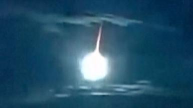 A white fireball with an orange tail illuminates an otherwise dark blue sky above Japan.