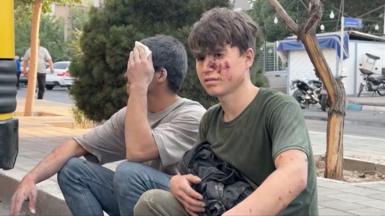 Two young men nurse injuries on a roadside in Iran.