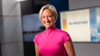 Ruth Dodsworth, with short blonde hair and wearing a pink top, stands in the ITV Wales studio smiling